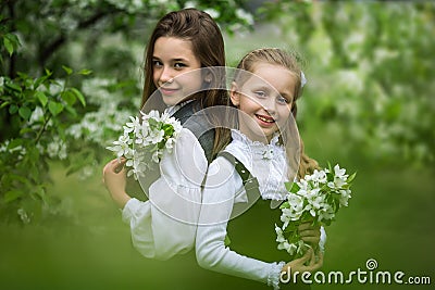 Two cute schoolgirl girls in an apple blossoming garden after school. End of school year Stock Photo