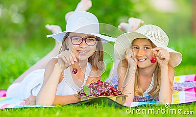 Two cute sisters or friends in a picnic garden lie on a deck and eat freshly picked cherries Stock Photo