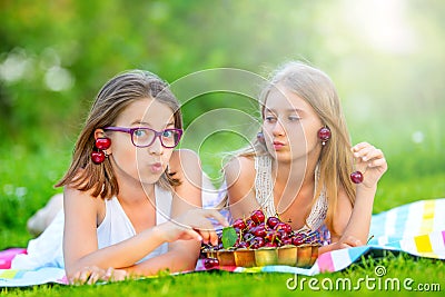 Two cute sisters or friends in a picnic garden lie on a deck and eat freshly picked cherries Stock Photo