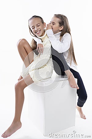 Two cute teenage girlfriends schoolgirls wearing white turtleneck sweaters, smiling sit back to back. on white. Fashion a Stock Photo