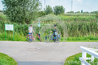 Two cyclists meet on road, one dressed in traditional Dutch costume the other with a red bicycle Editorial Stock Photo