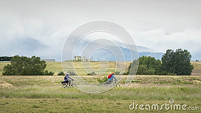 Two cyclists riding the Otago Rail Trail with clouds covering the mountains of picturesque Central Otago Editorial Stock Photo