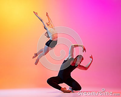 Two dancers, stylish sportive couple, male and female models dancing contemporary dance on colorful gradient yellow pink Stock Photo