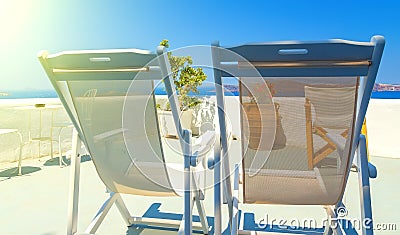 Two deckchairs on the roof of building on Santorini island, Greece. View on Caldera and Aegean sea, sunny day, blue sky. Stock Photo