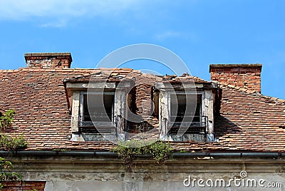 Two destroyed roof windows with rusted metal flower holders on abandoned old building with broken and missing roof tiles Stock Photo