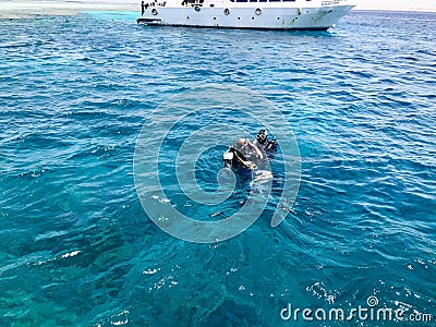 Two divers in black diving waterproof suits with shiny metal alluminium oxygen cylinders swim, immerse in blue sea water on vacati Editorial Stock Photo