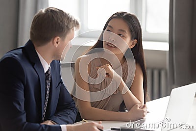 Two diverse colleagues talking sit at office desk with laptop Stock Photo