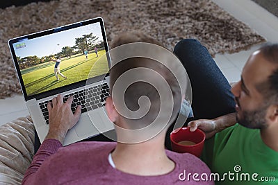 Two diverse male friends at home watching golf match on laptop Stock Photo