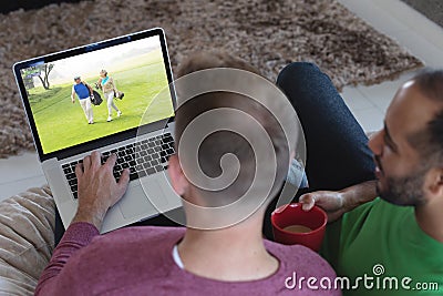 Two diverse male friends at home watching senior couple playing golf players on laptop Stock Photo