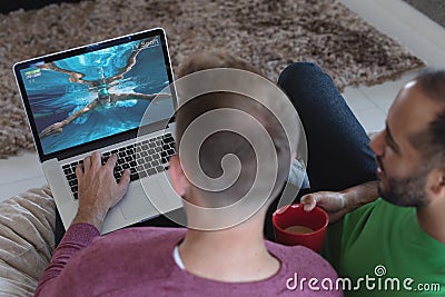 Two diverse male friends at home watching swimming competition on laptop Stock Photo