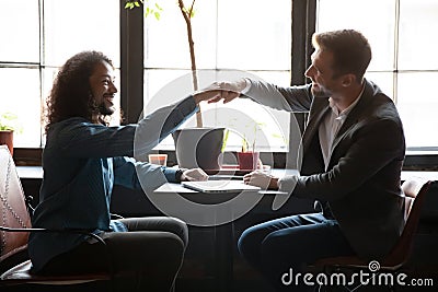 Two diverse men friends bumping fists above table at coffeehouse Stock Photo
