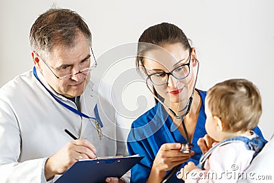 Two doctors examine a small child, one using a stethoscope and the other taking notes on a card Stock Photo
