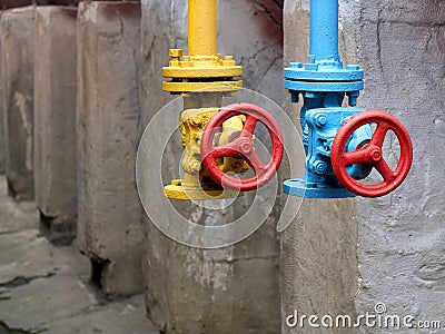 Two drain valves yellow and blue with red hand wheels over concrete elements and brown tanks background. Steampunk retro Stock Photo