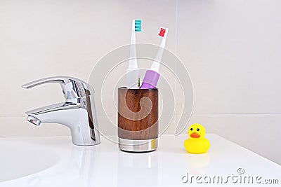 Two electric toothbrushes in wooden glass on sink in the bathroom Stock Photo