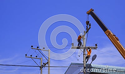 Two electricians with crane truck are installing electrical equipment on power pole against blue sky Editorial Stock Photo