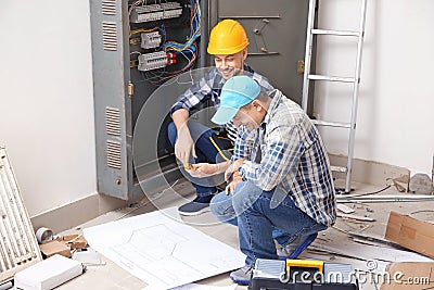 Two electricians with house plan near distribution board indoors Stock Photo