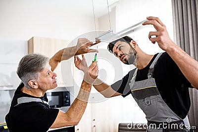 Two electricians, workers in uniform installing electric lamp, light inside apartment in the kitchen. Construction Stock Photo