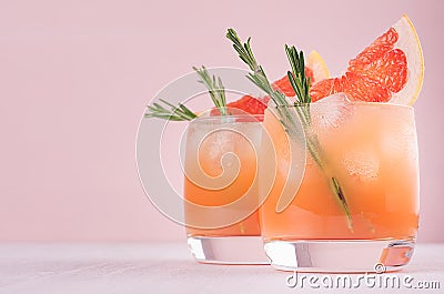 Two elegance cold wet drinking glasses with fresh grapefruit summer alcohol cocktail, ice, rosemary on fashion pink background. Stock Photo