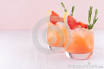 Two elegance cold wet drinking glasses with fresh grapefruit summer cocktail, ice, rosemary on pink background. Stock Photo