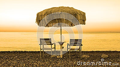 Two empty chairs stand on beach under open umbrella Stock Photo