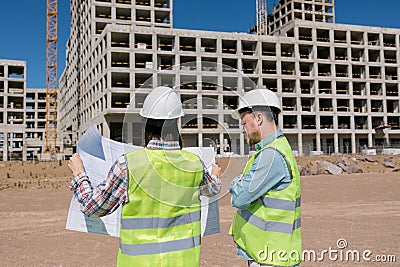 two engineers, a man and a woman in white helmets and protective vests, work at the construction site. Stock Photo
