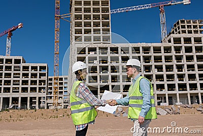 two engineers, a man and a woman in white helmets and protective vests, work at the construction site. Stock Photo