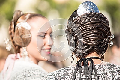 Two falleras talking. Detail of the hairstyle typical in this valencian celebration. Hair bun seen from behind Editorial Stock Photo