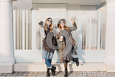 Two fashionable joyful smiling girls having fun on sunny street in city. Stylish look, travelling together, wearing Stock Photo
