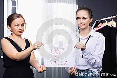 Two female consultants of fashion store holding Out of Stock placard. Clothing Store. Items out of stock Stock Photo