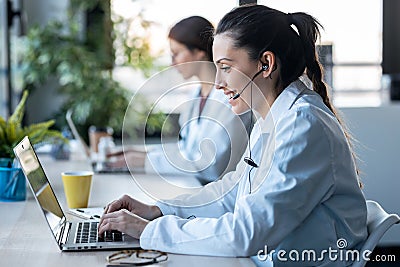 Two female doctor making video call with laptop while talking with earphone sitting in the consultation Stock Photo