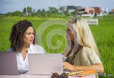 Two female friends caucasian and afro working together outdoors at cool internet cafe with laptop computer as digital nomad trave Stock Photo