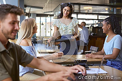 Two Female Friends At Table Meeting In Busy Coffee Shop Talking To Waitress Stock Photo