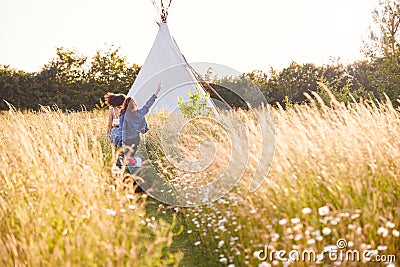 Two Female Friends Walking Pulling Trolley Through Field Towards Teepee On Summer Camping Vacation Stock Photo