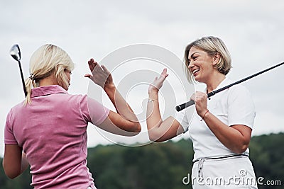 Two female golf players giving high five in the background of beautiful green woods Stock Photo