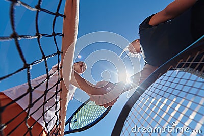 Two female tennis players shaking hands with smiles on a sunny day, exuding sportsmanship and friendship after a Stock Photo
