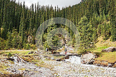 Two female trekkers with backpack crossing bridge. Women hikers backpackers. Karakol valley on trail to Ala Kul lake. Karakol Stock Photo