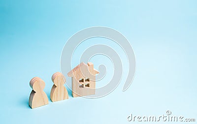 Two figures of people and a wooden house on a blue background. The concept of affordable housing and mortgages for buying a home Stock Photo