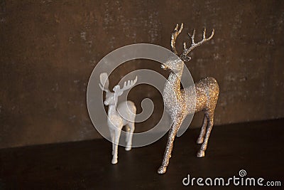 Two figurines of deer - small white and big gold color - stand on a brown table Stock Photo