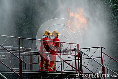 Two firefighter try to extinguish or get rid of fire from gas pipe on top of building and they protech themselves by using water Stock Photo