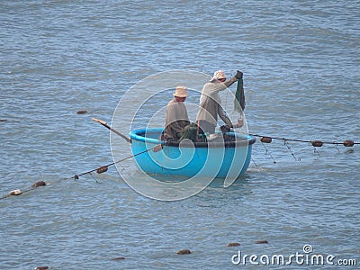 Two fishermen sail in a traditional Vietnamese boat. One of them throws the net Editorial Stock Photo