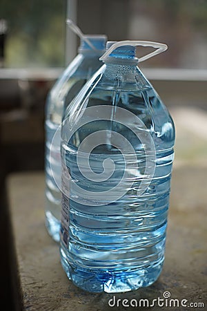 Two five-liter plastic bottles full of water on the table, side Stock Photo