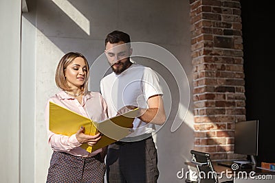 Two focused coworkers, woman and man, looking through documents from folder standing in office Stock Photo