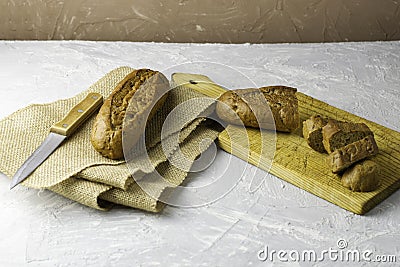 two fresh rye buns on a cutting wooden board and a piece of burlap one of the buns is cut there is a knife next to it Stock Photo