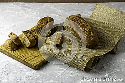 two fresh rye buns on a cutting wooden board and a piece of burlap one of the buns is cut there is a knife next to it Stock Photo