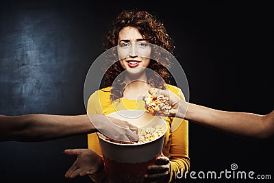 Two friends taking popcorn from girl`s bucket. Negative facial emotions Stock Photo