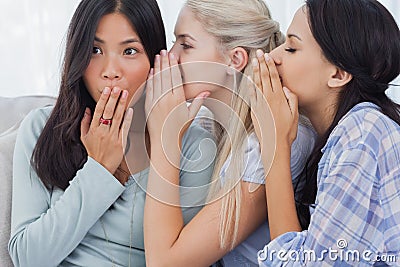 Two friends whispering secrets to shocked brunette Stock Photo