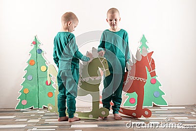 Two funny boys in a Santa Claus hat are playing with horses drawn on cardboard. The guys have fun at home. Christmas holiday conce Stock Photo