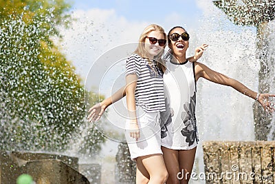 Two Funny and Laughing Teenage Girlfriends Embracing Together. Posing Against Fountain in Park Outdoors Stock Photo