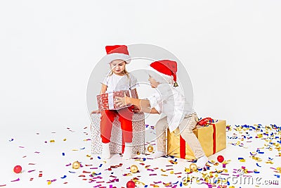 Two funny little kids in Santa hat sitting on gift boxes. Isolated on white background, confetti on a floor. Christmas and new Stock Photo