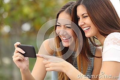 Two funny women friends laughing and sharing media in a smart phone Stock Photo